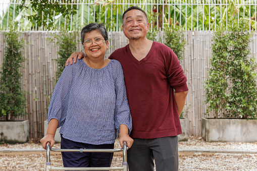 A joyful Asian senior woman stands confidently outdoors with a quad cane, while an elderly couple stands side by side, wrapping shoulders together, radiating happiness. healthy elderly individuals.