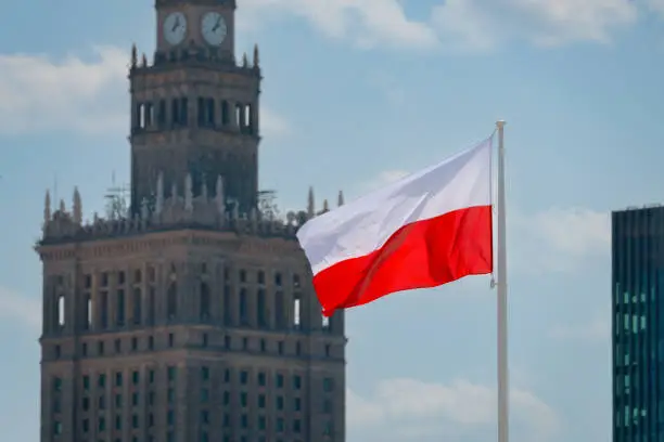 Photo of Flag of Poland waving at wind against beautiful blue sky and Palace of Culture and Science