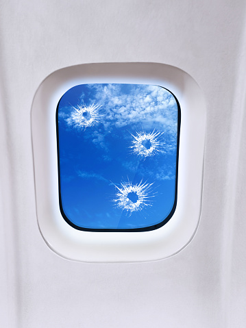 Airplane window with bullet holes, sky view and clouds
