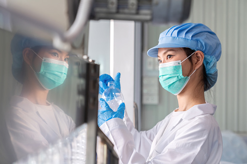 Meticulous world of quality control as a skilled worker woman in lab coat inspect every plastic bottle before filling water in the water factory. Ensures that only the highest standards are met. Fusion of technology, manufacturing expertise, and dedication to excellent