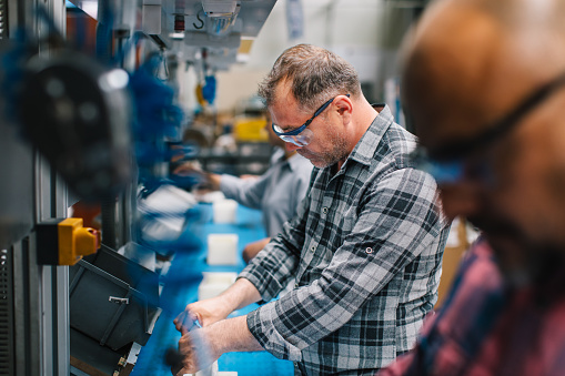 Concentrated professional young industrial factory workers men working with machine parts hands using electric pneumatic screwdriver retractable mechanism, fastened with screws in large Electric electronics wire and cable manufacturing plant factory warehouse