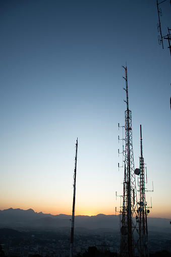 radio and television telecommunication antenna towers with parabolic sunset or sunrise in mountain city background portrait