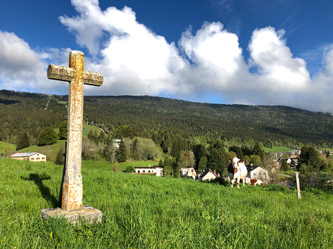 Meaudre, Le Vercors, France: One of the crosses on the stations of the cross near the Eglise Saint-Pierre-et-Saint-Paul in Meaudre, with a cow and the village of Meaudre in the background.