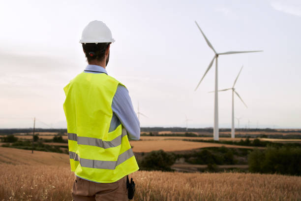 istock Engineer back turned looking at wind farm installations in open field. Qualified energy worker. 1517852532