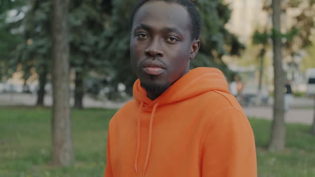 Slow motion portrait of emotionless African American man in hoodie standing outdoors against city background