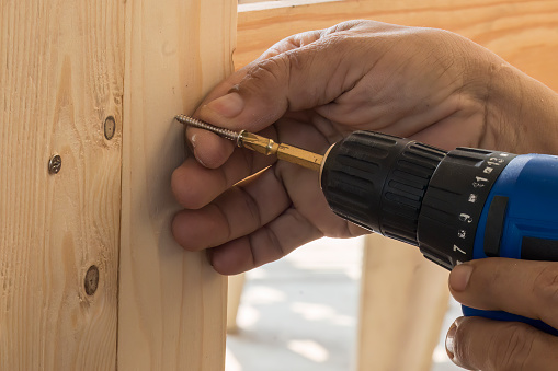 The carpenter using the cordless screwdriver with wood board. The carpenter assembly the wood furniture by screw driver.