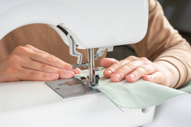 istock Female hands stitching white fabric on modern sewing machine at workplace in atelier 1518019674