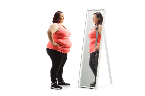 Overweight woman looking at a slimmer version of herself in the mirror isolated on white background