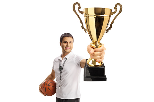 Basketball coach holding a ball and showing a gold trophy cup isolated on white background