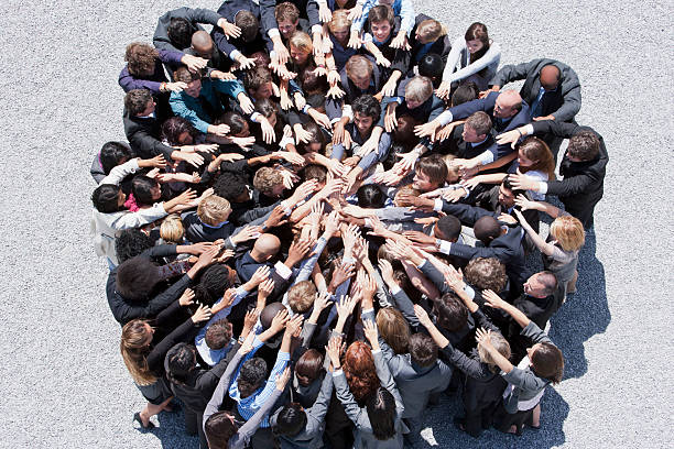 Crowd of business people forming huddle with extended arms  dedication stock pictures, royalty-free photos & images