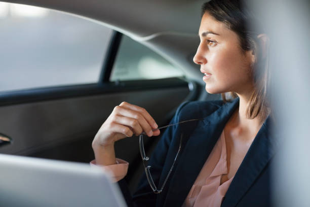 pensoso donna d'affari con computer portatile nel sedile posteriore dell'auto - abbigliamento elegante foto e immagini stock