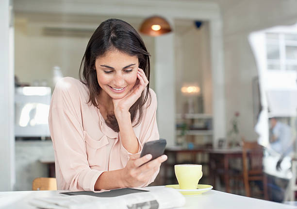 sonriendo empresaria mirando hacia abajo en teléfono celular en café ventana) - mujer leyendo periodico fotografías e imágenes de stock