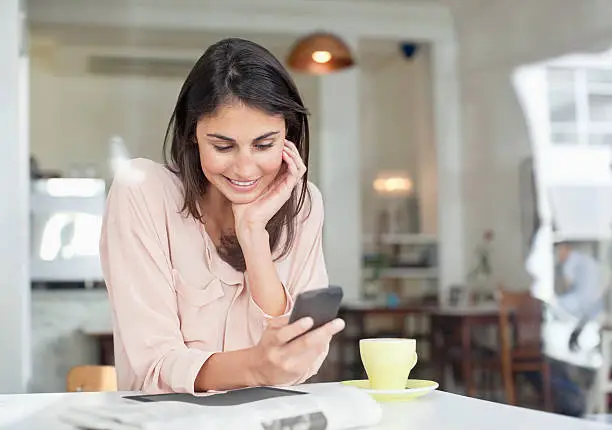 Photo of Smiling businesswoman looking down at cell phone in cafe window