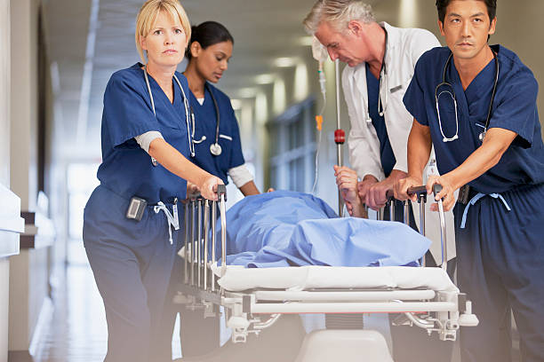 Doctor and nurses wheeling patient in gurney down hospital corridor  emergency room photos stock pictures, royalty-free photos & images