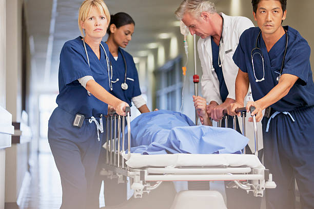 doctor and nurses wheeling patient in gurney down hospital corridor - emergency room ภาพสต็อก ภาพถ่ายและรูปภาพปลอดค่าลิข�สิทธิ์