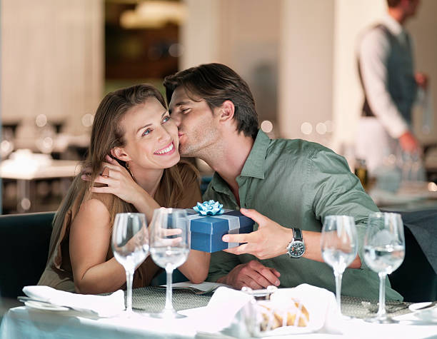 Man kissing and giving gift to woman in restaurant anniversary gifts stock pictures, royalty-free photos & images