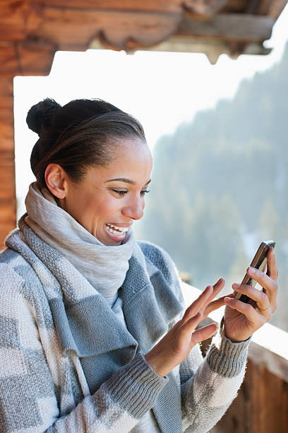 souriant femme vérifiant son téléphone cellulaire sur la cabine porche - telephone cabin photos et images de collection