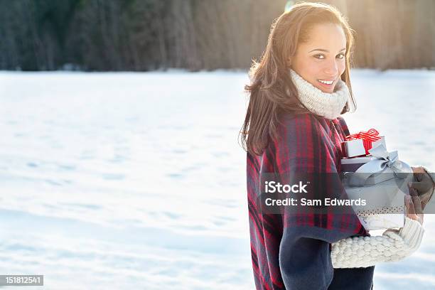 Portrait Of Smiling Woman Carrying Christmas Gifts In Snow Stock Photo - Download Image Now