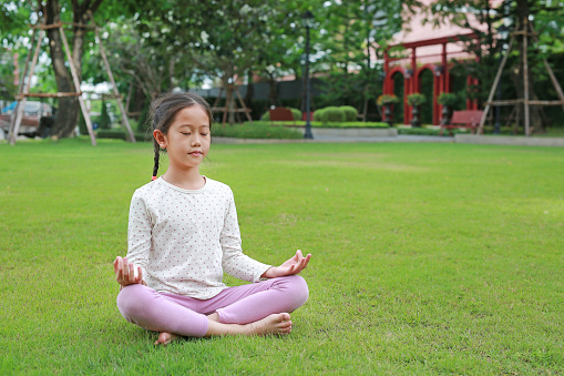 Asian young girl child practicing mindfulness meditation sitting on lawn in the garden. Peaceful concept.