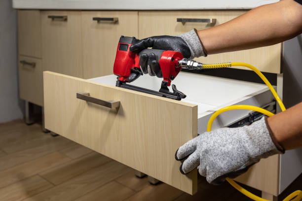 Worker repair wooden drawer of cabinet with pneumatic nail gun. stock photo