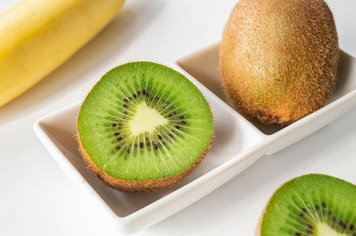 Fresh brown kiwi cut in half with green flesh in a small square cup. on a white background