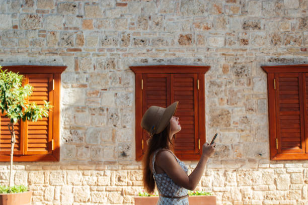 a girl in a hat with long hair and in a dress, with a phone in her hands on vacation