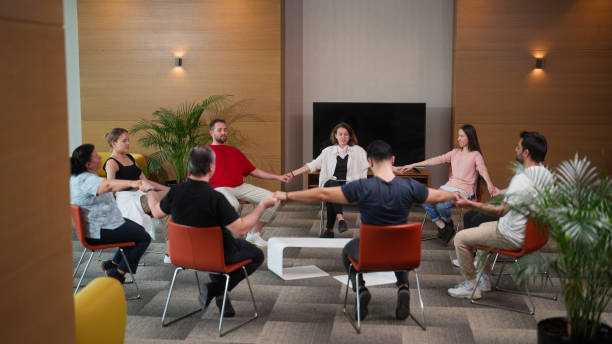 Group therapy professional leading group therapy session and meditating A female group therapy professional is leading a group therapy session and meditating. nervous holding hands stock pictures, royalty-free photos & images