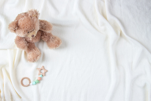Teddy bear and natural wooden rattle toy on white blanket throw background. Top view.