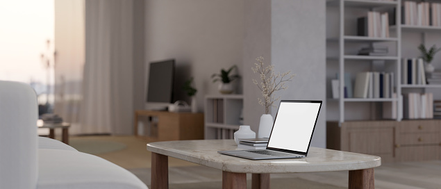 Close-up image of a laptop computer white screen on a coffee table in a modern contemporary living room. 3d render, 3d illustration