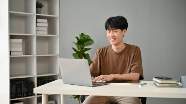 istock A happy and handsome young Asian man using his laptop in his home office. 1518569503