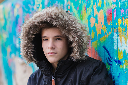 Teenager in hoodie on the street leaning against a wall, looking at the camera