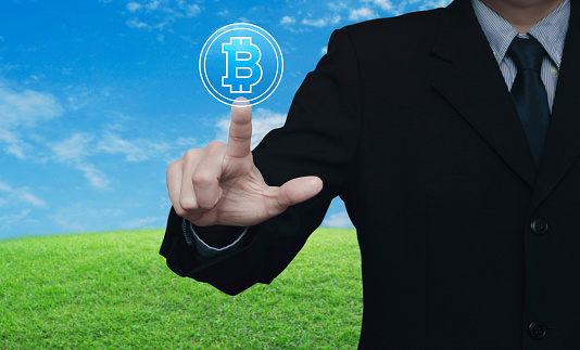 Businessman pressing bitcoin icon over green grass field with blue sky, Choosing bitcoin concept