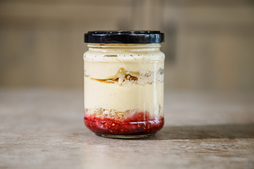 Raspberry vanilla ice cream trifle unevenly layered in a jar with tap on the counter, sweet food