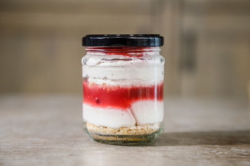 Strawberry vanilla ice cream trifle unevenly layered in a jar with tap on the counter, sweet food