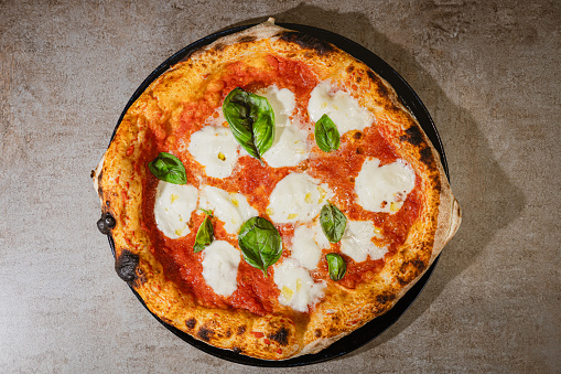 Directly above round freshly baked pizza Margherita on the counter, tomato sauce, basil leaves and mozzarella, savory food