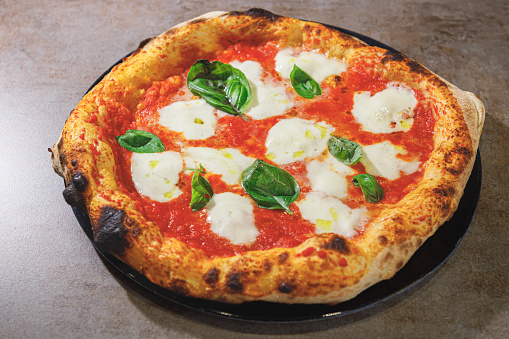 Round freshly baked pizza Margherita on the counter, tomato sauce, basil leaves and mozzarella, savory food