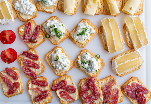 Delicious homemade platter with crackers. Topped with a variation of cheese and salami. Closeup, flat lay background.