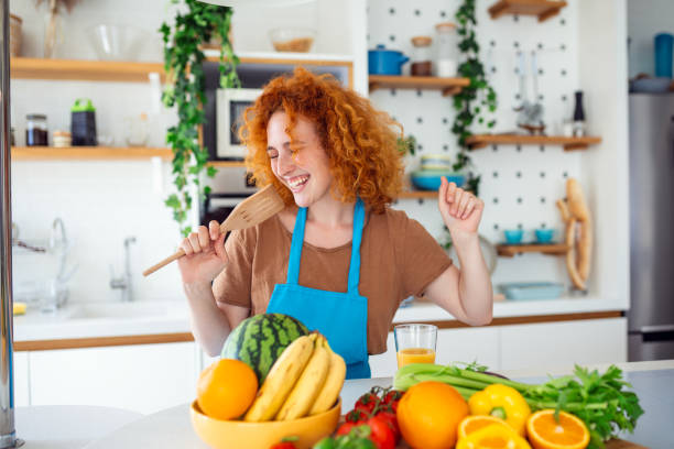istock Woman joyfully sings, using a wooden spatula as a microphone. Her carefree expression and melodious voice fill the space with music, capturing the essence of happiness and culinary creativity 1518653245