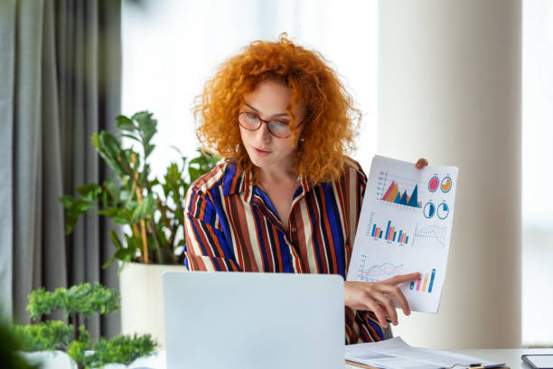 A red-haired businesswoman confidently presents data and analytics in a video call. With expertise and visuals, she embodies professionalism, capturing impactful virtual presentations in this image