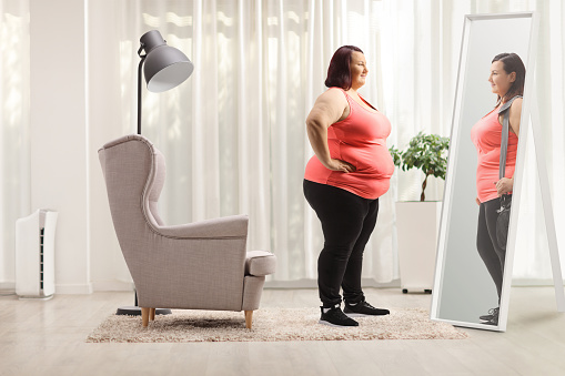 Overweight woman looking at a slimmer version of herself in the mirror at home