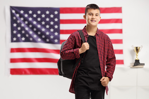 Teenage boy with a backpack smiling at the camera in front of a USA flag