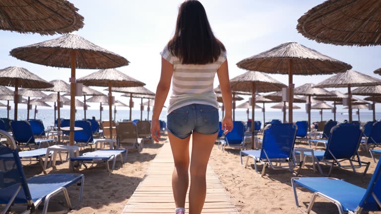 Woman Walking Among Beach Lounge Chairs And Parasols