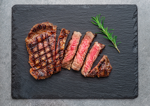 Grilled  delicious ribeye steak slices and rosemary twig on black slate serving plate. Flat lay.