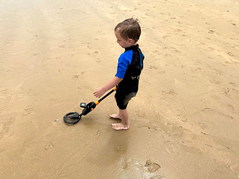 a boy looking for treasures on the beach, with a metal detector