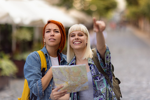 Happy female friends analyzing a city map while blond woman is showing their direction.