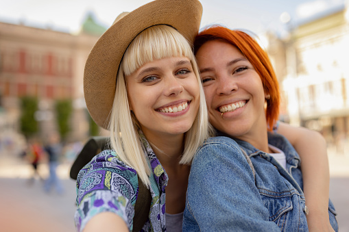 Happy female couple of tourists having fun while taking a selfie in the city and looking at camera.