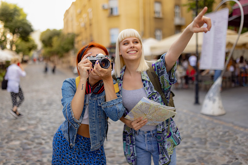 Happy female tourist showing her friend what to photograph during city exploration.