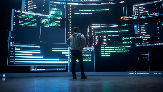 Back View of Young Black Man Standing and Looking at Big Digital Screens Glitching While Displaying Code Lines. Professional Hacker Breaking Through Cybersecurity Protection System, Changing Code