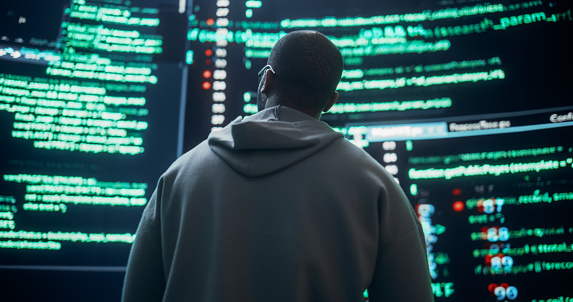 Back View of Young Black Man Looking at Big Digital Screens Glitching While Displaying Code Prompts. Worried Professional Programmer Fixing a Bug, Dealing with Crashing System, Ensuring Cybersecurity