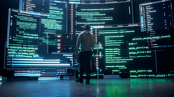 Back View of Young Black Man Walking and Looking at Big Digital Screens Glitching While Displaying Code Lines. Professional Hacker Breaking Through Cybersecurity Protection System, Changing Code